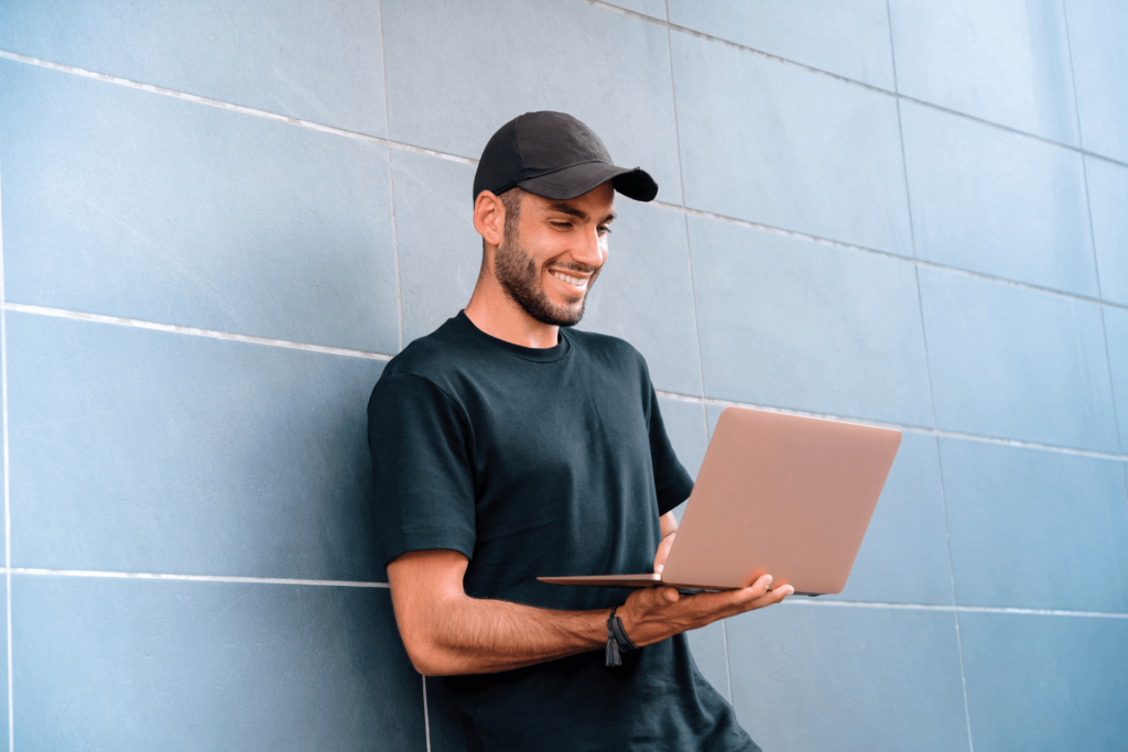 Man leaning against wall looking at laptop